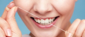 Part of female face. Young woman smiling girl cleaning her white teeth with dental floss on blue. Daily health care. Studio shot.
